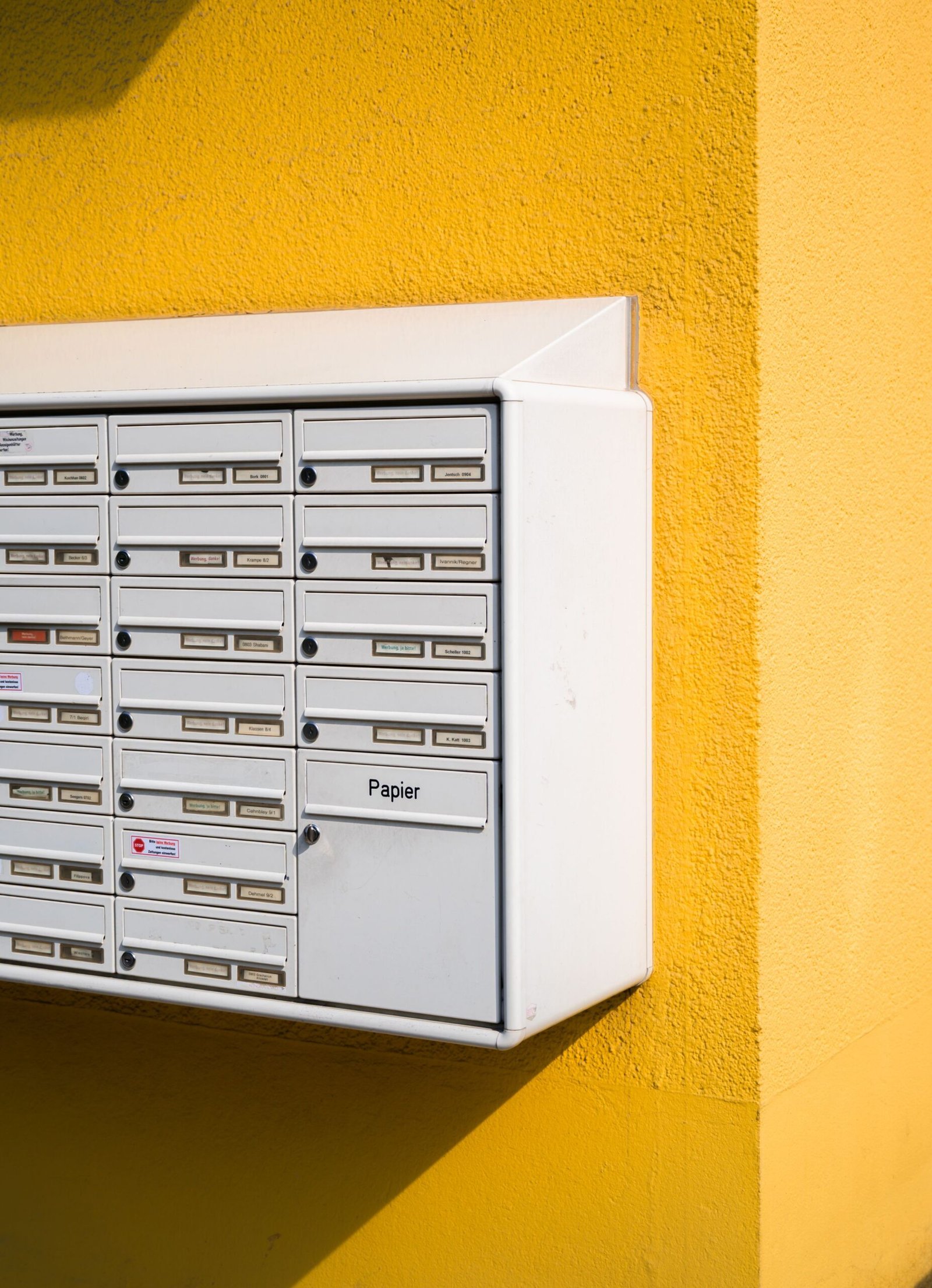 White mailbox against a vibrant yellow wall, showcasing urban architecture.